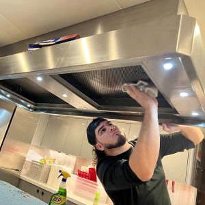 Technician cleaning stainless steel kitchen hood in a marine appliance setting, highlighting professional maintenance services offered by Appliances of Broward.