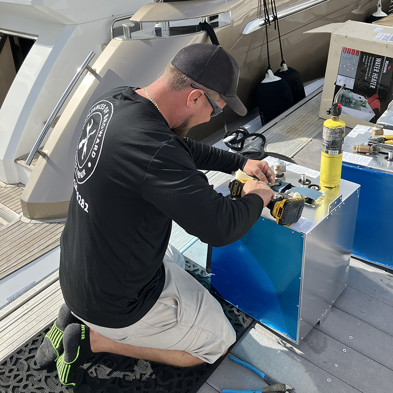 Technician installing marine water heater on yacht deck, featuring tools and equipment for appliance repair.